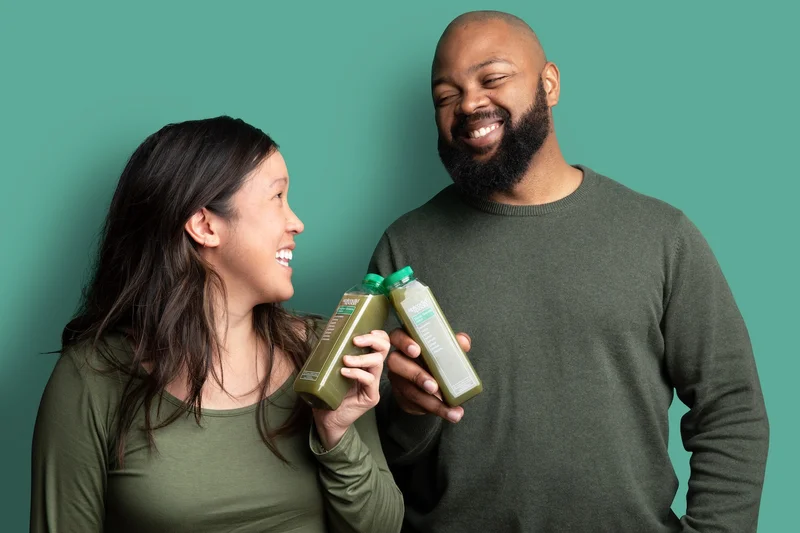 Two people holding Splendid Spoon green juices, cheering