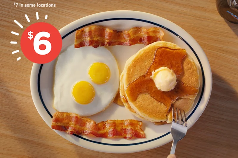 The Breakfast Faves Combo, with two buttermilk pancakes topped with butter and syrup, two bacon strips, and two eggs sunny side up.