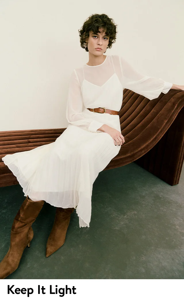A woman wearing a white dress with a sheer top and pleated skirt.
