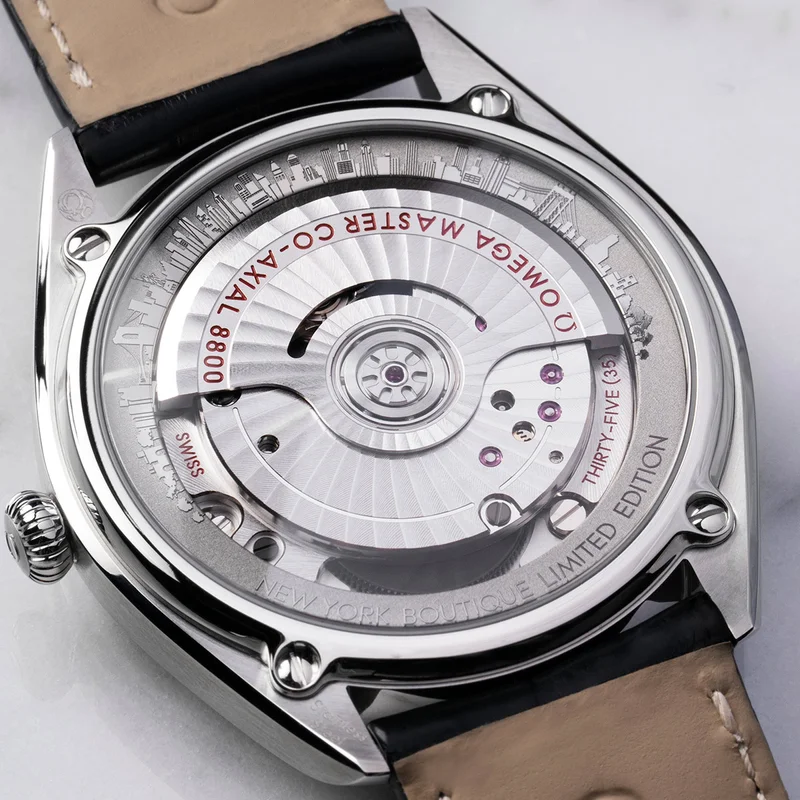 The back of a Seamaster watch, showcasing its open case back with a detailed view of the movement and a laser-engraved cityscape of iconic New York locations.
