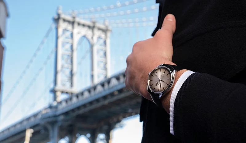 A man in a suit wearing a limited OMEGA Seamaster watch, with the blurred background of the Manhattan Bridge in New York.