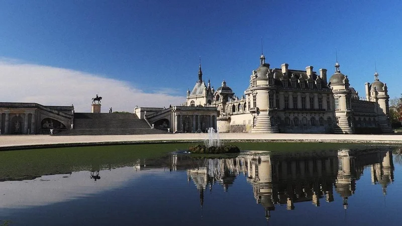 Image description: Exterior view of Château De Chantilly with pond in foreground.