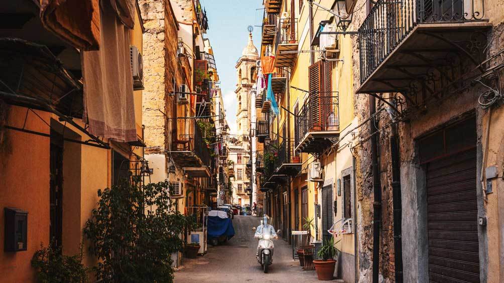 Image description: A person rides a moped down a side street in Palermo, Sicily.