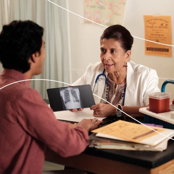 A doctor sitting at a desk talking to a patient sitting across from her while holding up a scan to show her.