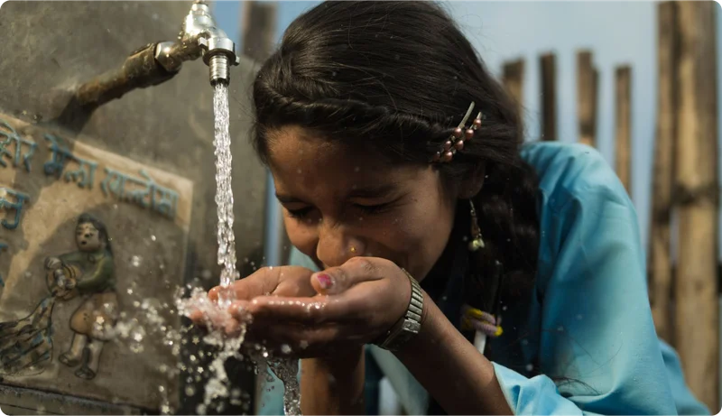 A girl cups her hands and drinks water as it comes out of a faucet.