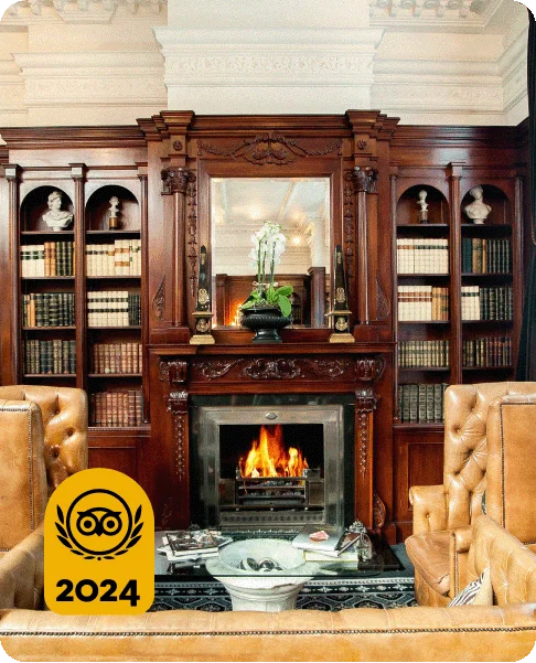 Image Description: A dark wood fireplace and bookshelf in a cozy lounge with leather chairs. A gold 2024 Travelers’ Choice Awards Best of the Best badge is on the bottom left corner of the image.