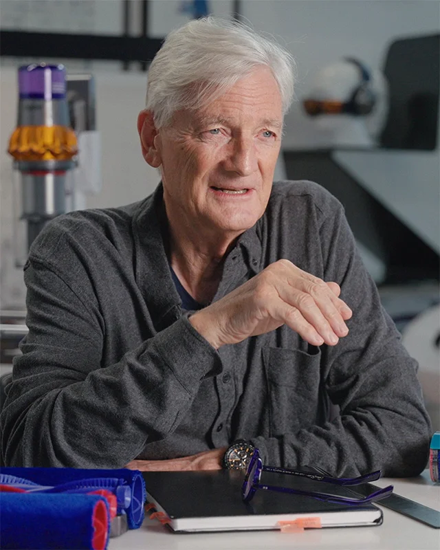 James Dyson sitting in his office, surrounded by Dyson products and parts