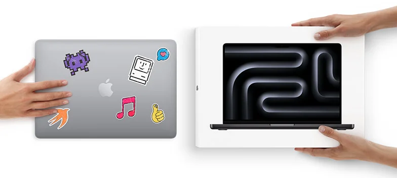 A hand slides a MacBook with stickers on the cover toward two hands holding a new MacBook in the box