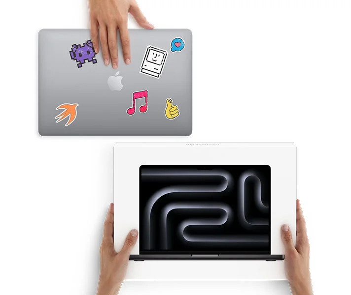A hand slides a MacBook with stickers on the cover toward two hands holding a new MacBook in the box