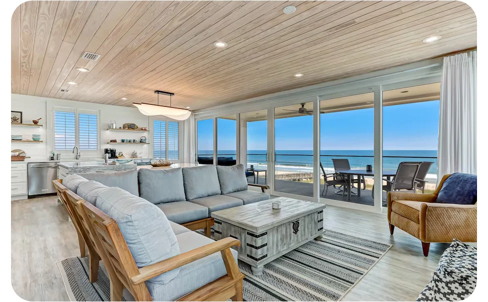 Open living area with seating and a kitchen, extending to a balcony with outdoor chairs and ocean views.