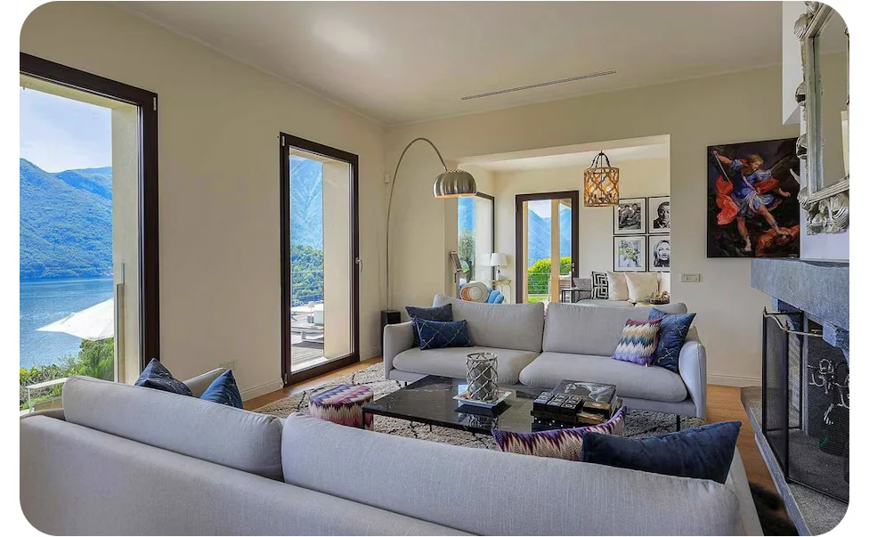 Living area with seating and large windows, showing views of a lake and surrounding hills.