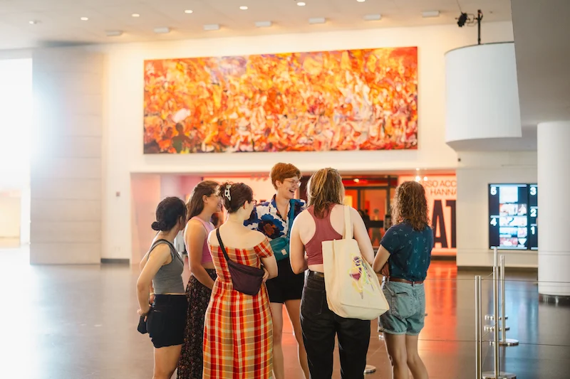 A photograph of people standing in a circle and talking in the Brooklyn Museum lobby