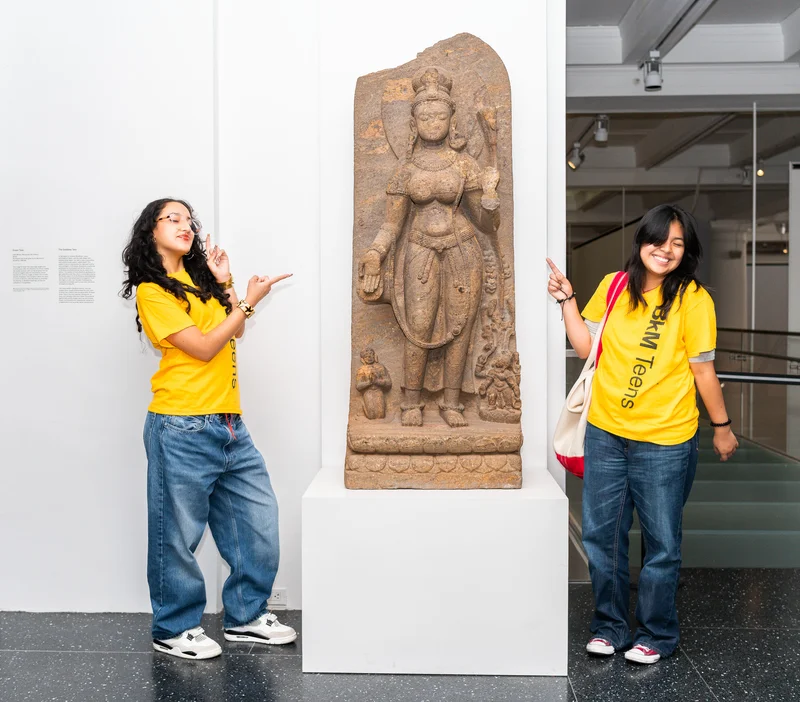 A photograph of smiling teens pointing to art in the gallery