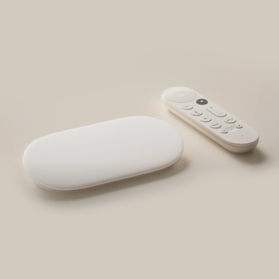 A pill-shaped, white device — the Google TV Streamer — sits on a surface next to a smaller, white, pill-shaped remote.