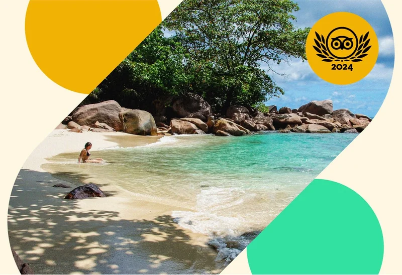 Image Description: A person sitting in the ocean on a sandy beach surrounded by rocks and green trees. A gold Travelers’ Choice Awards Best of the Best 2024 badge is on the top right corner.