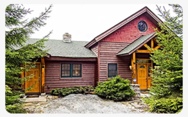 Rustic wood cabin with pitched roof, timber details, and evergreen trees surrounding it.