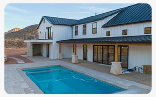 Modern desert home with metal roof, stone columns, sliding doors, and a rectangular pool.