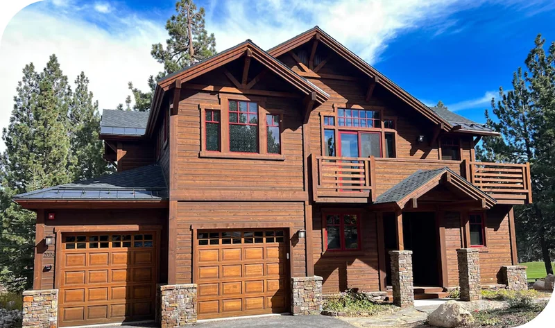 Wood-clad mountain home with balconies, stone accents, and pine trees.