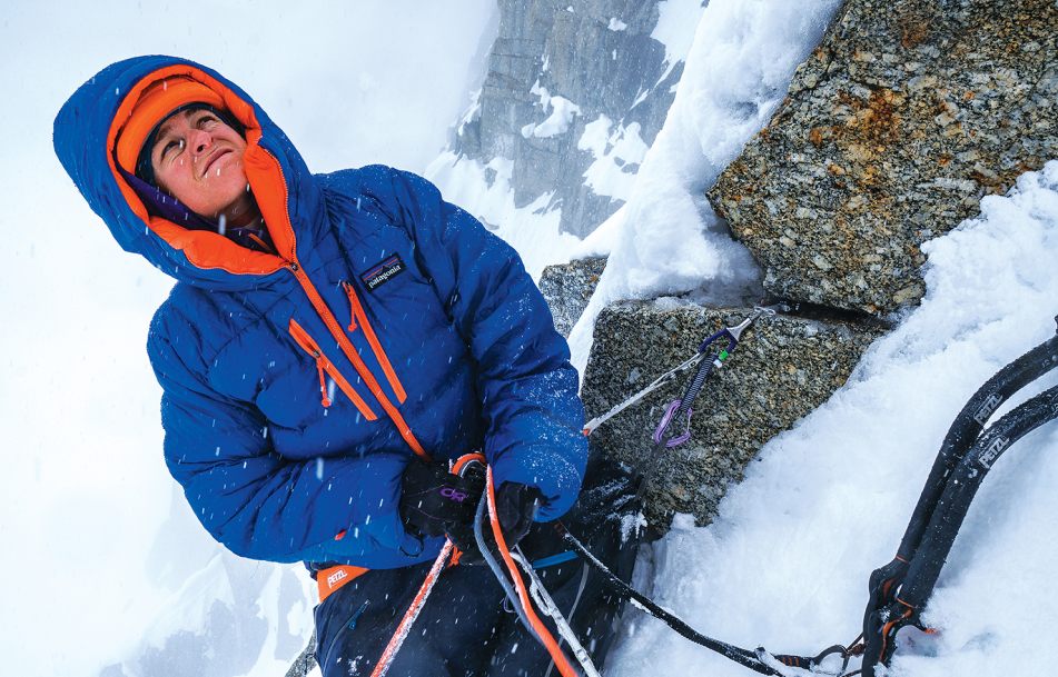 An alpine climber belays their partner on a snowy mountain.