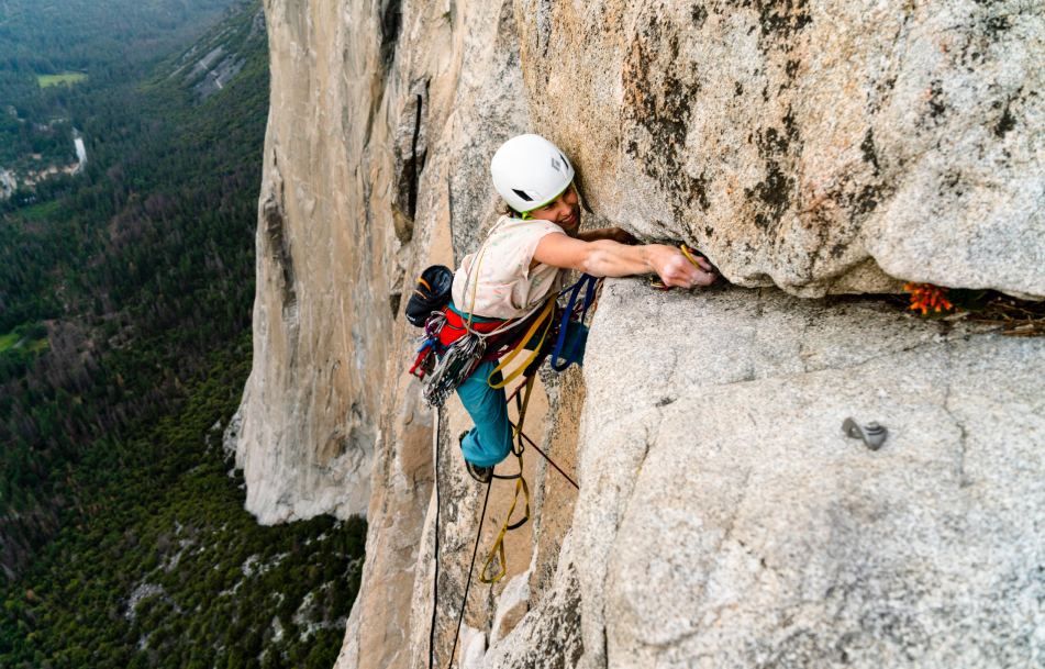 A climber high on a big wall reaches to place a piece of protection.