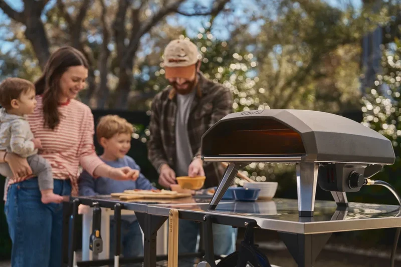A family making a pizza, standing around a Koda 2 in a garden.
