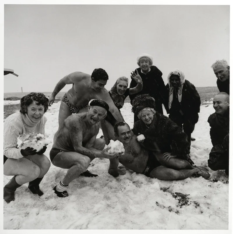A group of people in swimsuits holding snow on the beach