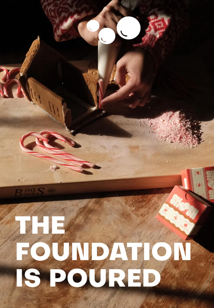 Gingerbread house being built with the text THE FOUNDATION IS POURED on it