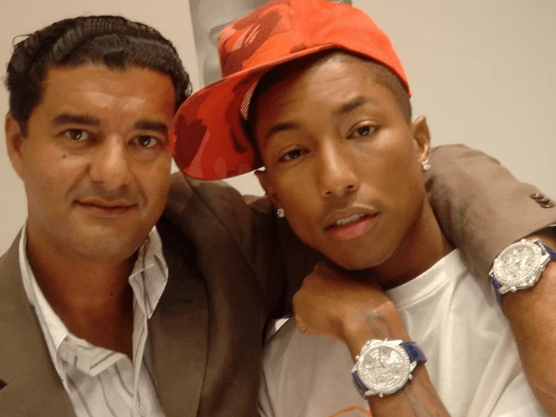 Image may contain: Pharrell Williams, Baseball Cap, Cap, Clothing, Hat, Body Part, Finger, Hand, Person, and Accessories