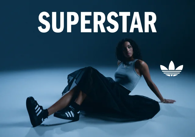 Woman posing on the ground wearing adidas superstar sneakers. Superstar text overlay at the top.