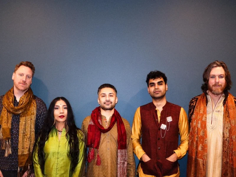 A group of five people standing against a blue wall