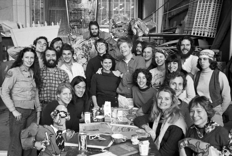 A group of people clustered around a table surrounded by puppets