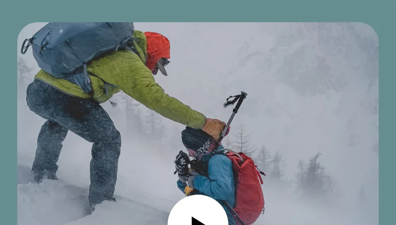 A grown-up helps a kid get their hood up during a blizzard.