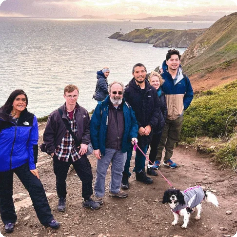 Image Description: A group of people and a dog standing on a cliff near the water.