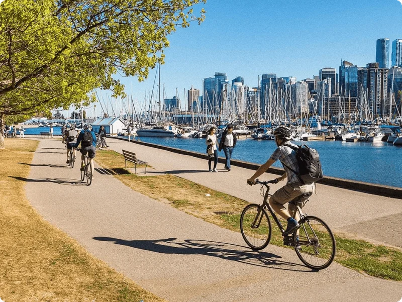 Image Description: Travelers cycling along the famous Vancouver Seawall in Stanley Park, against a backdrop of yachts and skyscrapers