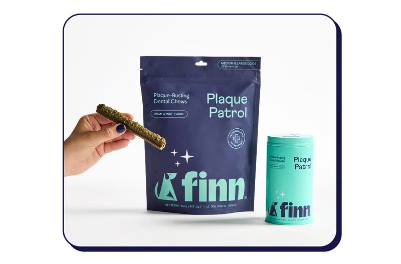 Image of Dental chews next to a tin of dental powder. A hand is holding a chew with the powder in paste form in its groove