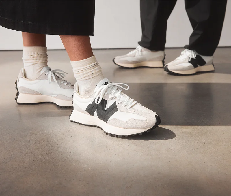 A stack of New Balance shoe boxes next to a shopping bag against a pale apricot backdrop