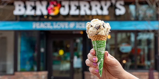 Hand holding an ice cream cone in front of a Ben & Jerry's Scoop Shop.