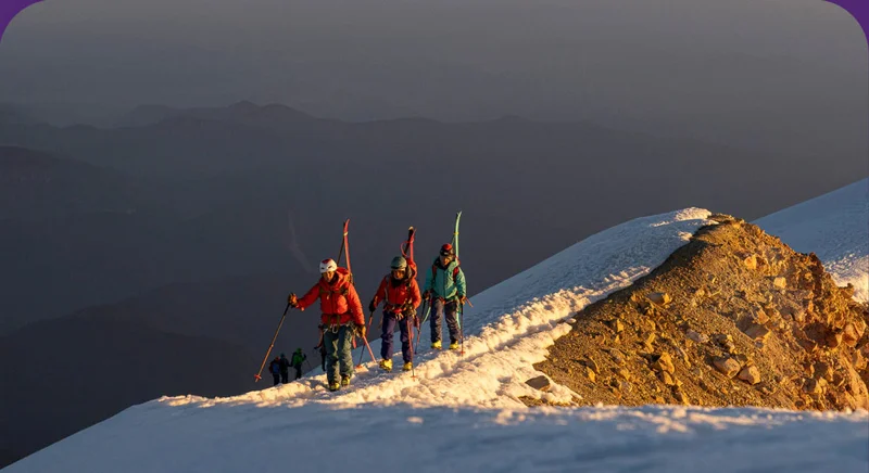 A group of people walking up a mountain with skis on their backs.