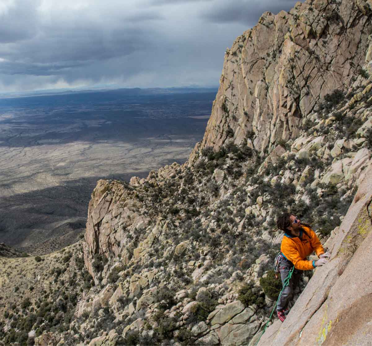 A rock climber scaling a route with a large view of the desert behind them.