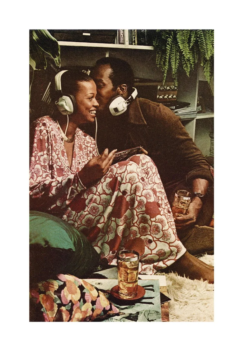 Photograph of two people in headphones, one kissing the other's cheek