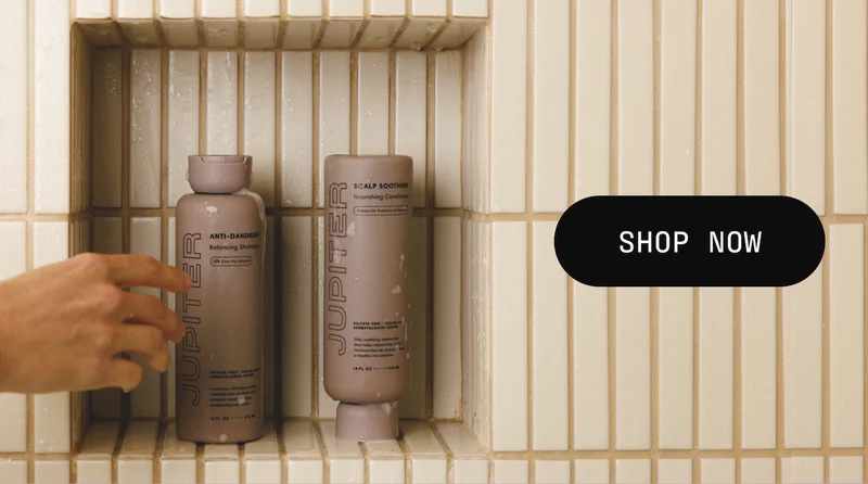 Hand reaching for Jupiter Anti-Dandruff Shampoo and Scalp Soothing Conditioner on a shower shelf. Button: Shop now.