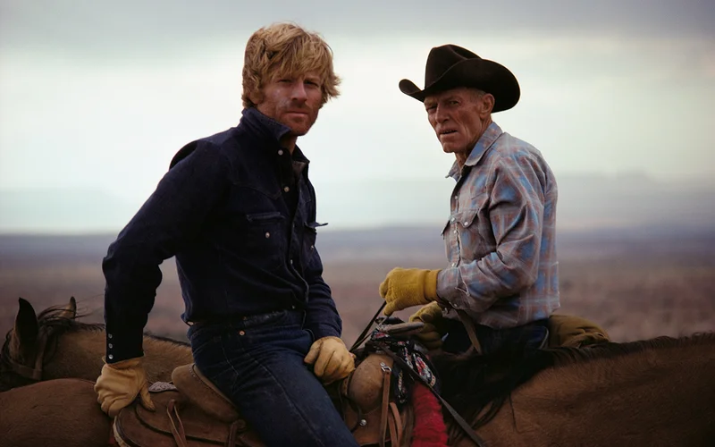 Robert Redford and companion sit astride horses.