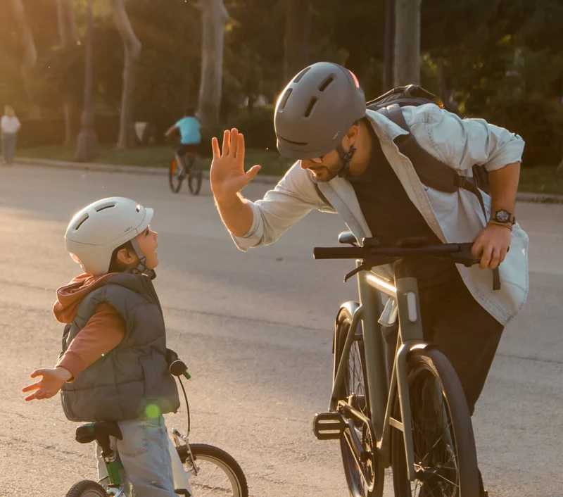 A man riding his bike in the park with his son, both wearing a smart helmet to be safe in the road.