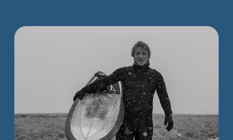 A person in a wetsuit holding a surfboard on a snowy day.