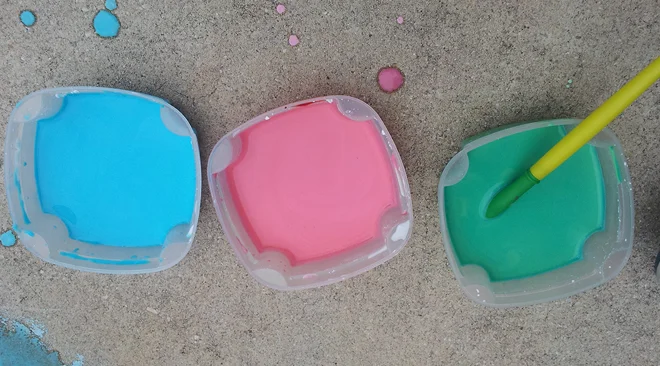 Three bowls of colorful homemade chalk paint with a paintbrush on concrete.