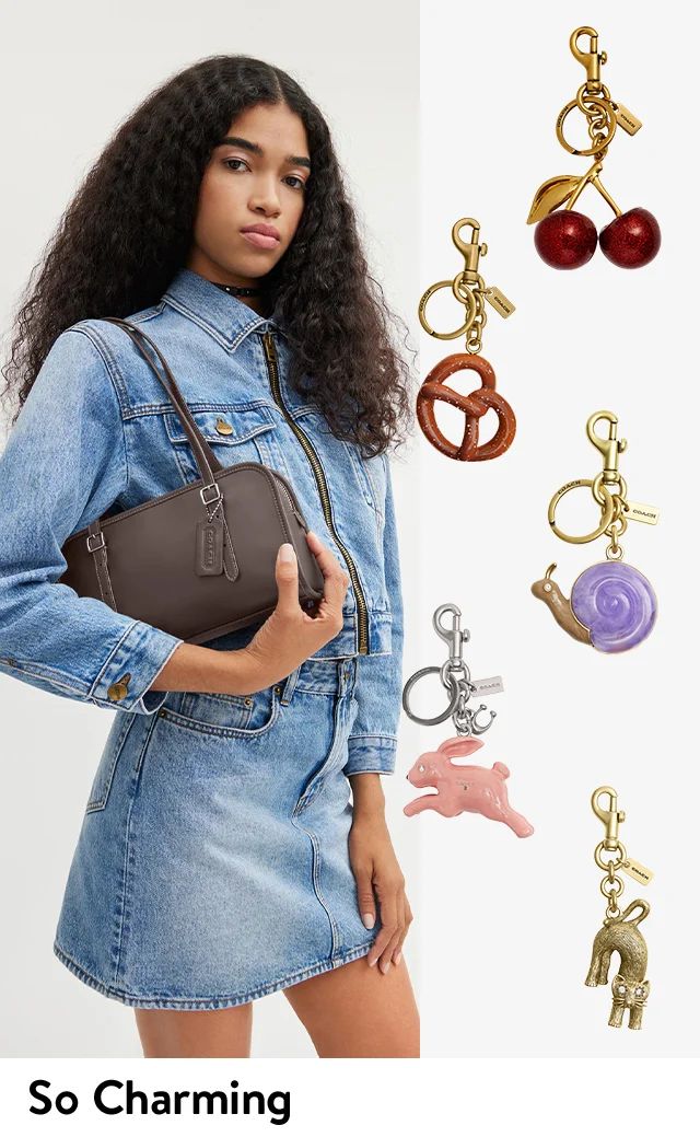 A woman holding a shoulder bag. Cat, pretzel, cherry and snail bag charms.