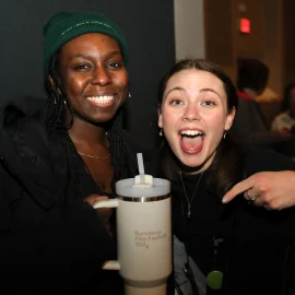 Two smiling women, holding and pointing to a Sundance Film Festival tumbler.