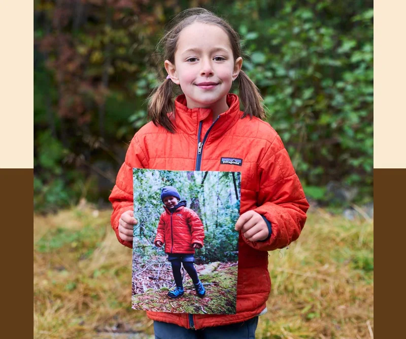 A young person in a red Nano Puff jacket holds a photograph of herself as a little kid wearing the same jacket.
