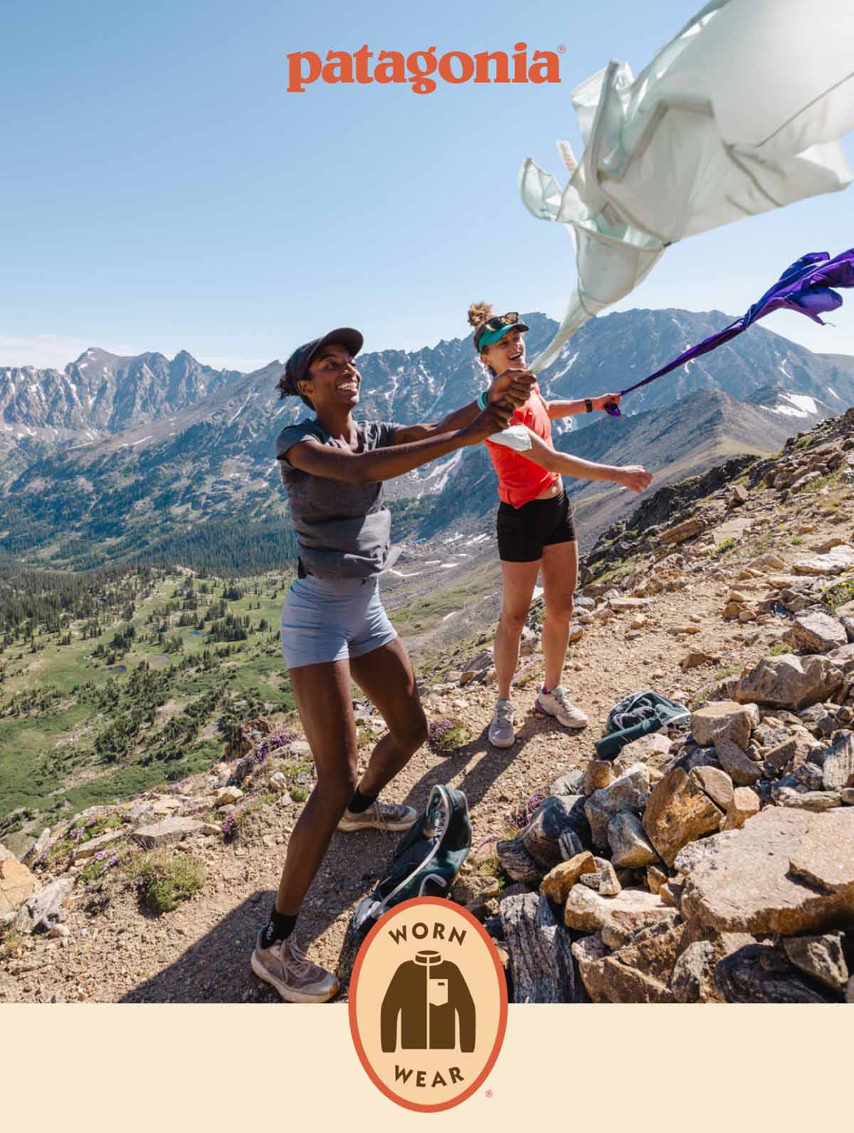 Patagonia. Two runners fly their windbreakers like kites on a windy day on an alpine trail. Worn Wear Logo