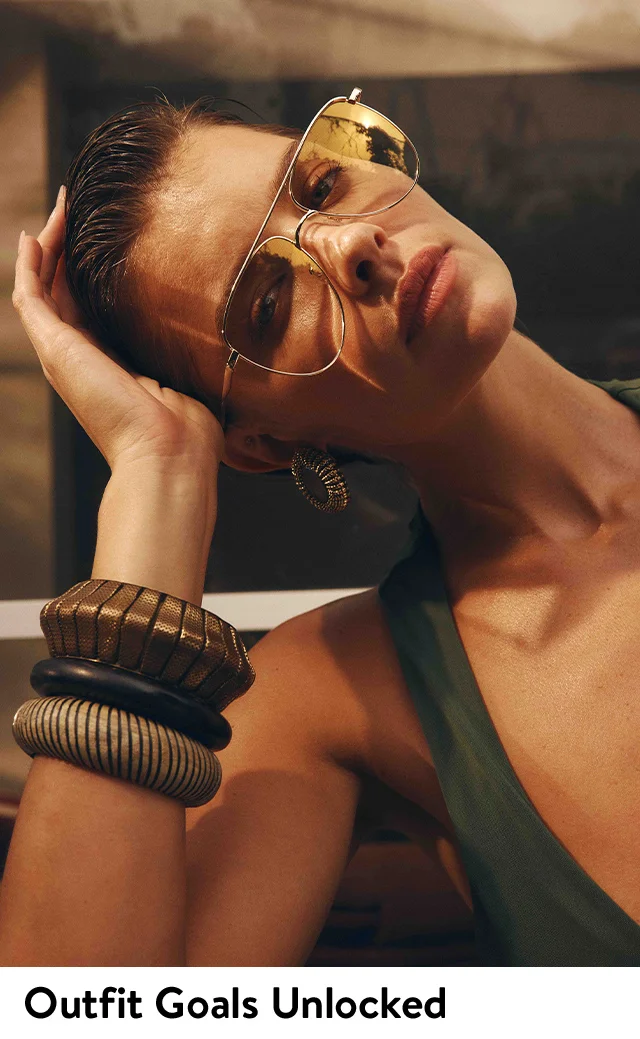 A woman wearing aviator sunglasses and chunky bangles.